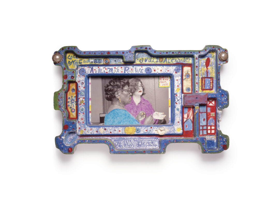 A black-and-white photo of Nellie Mae Rowe and Judith Alexander—colored with blue, purple, and yellow accented lips, garments, jewelry, and fingernails—housed within an ornate Styrofoam frame with text “Call on God” and “Judith Alexander.”